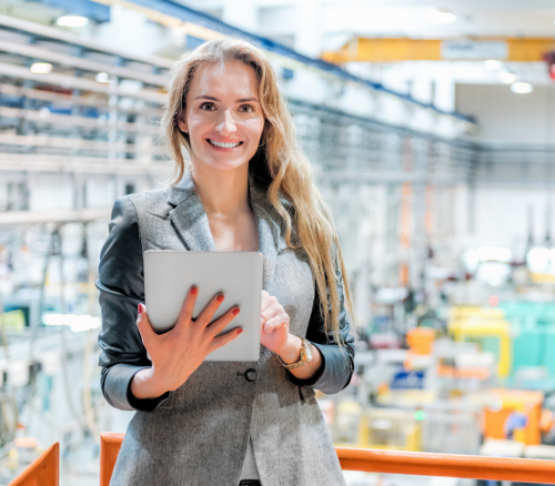 a woman holding a tablet and standing on a balcony overlooking a manufacturing plant that uses diamond ai for manufacturing